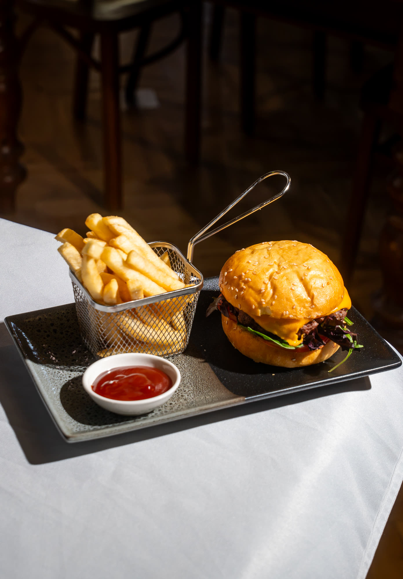 A cheeseburger with a basket of fries and a dish of tomato sauce.