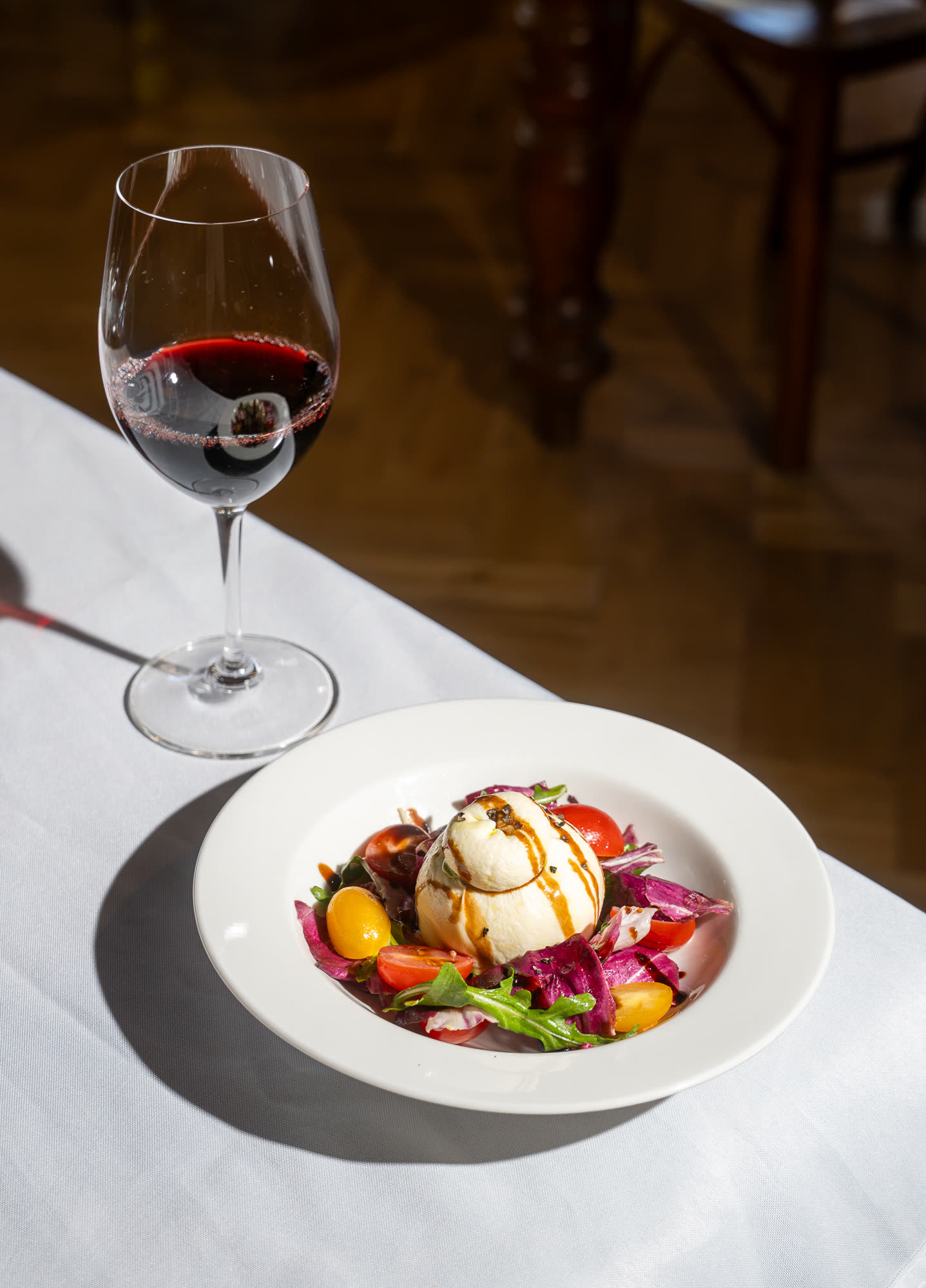A burrata salad with cherry tomatoes and radicchio, served with a glass of red wine.