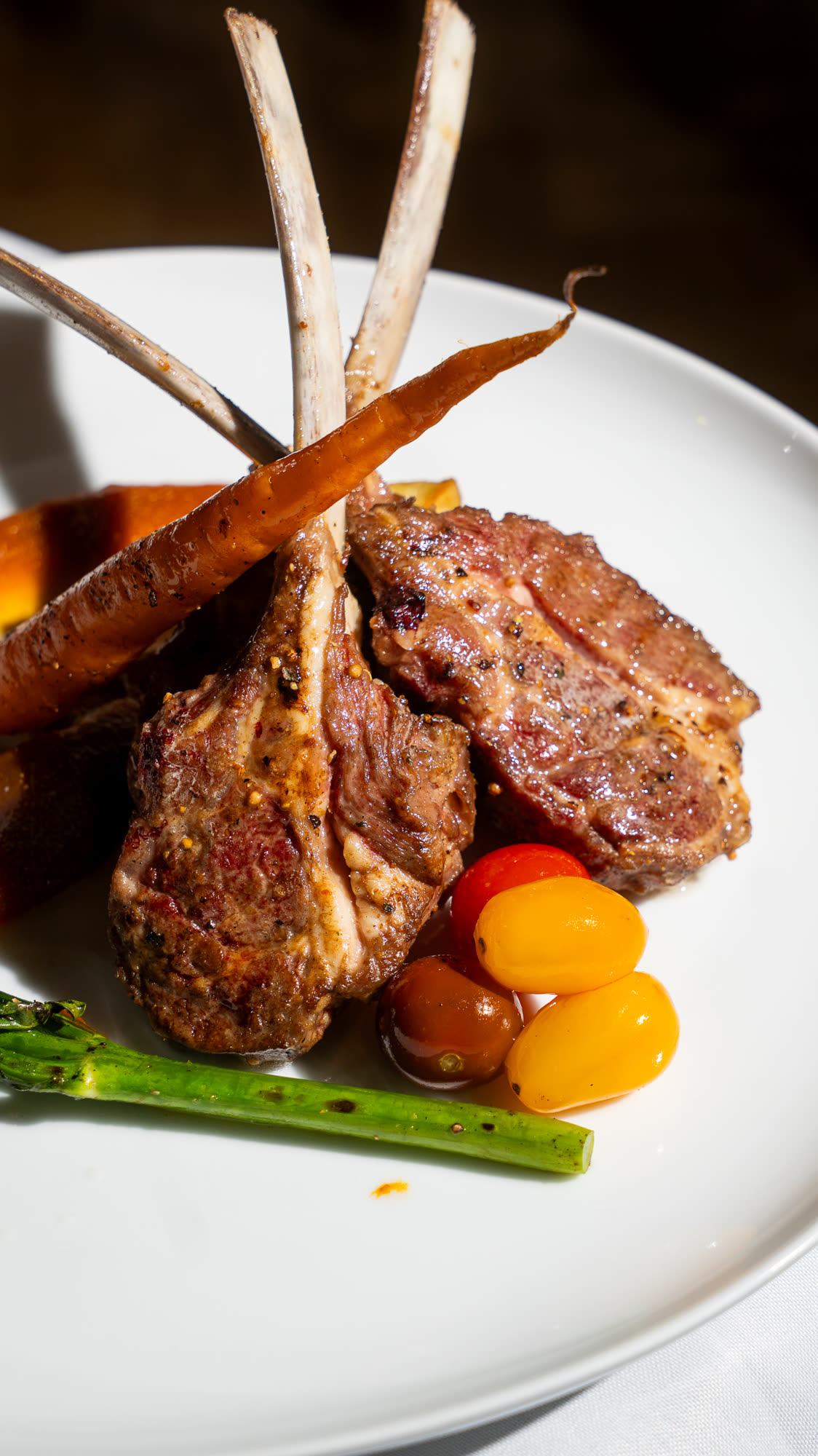Plated lamb cutlets with a glazed carrot, broccolini and cherry tomatoes.