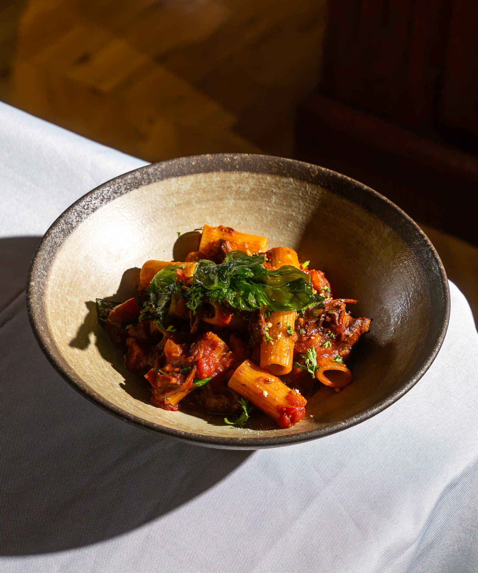 A bowl of rigatoni in a rich tomato sauce, topped with fresh herbs.
