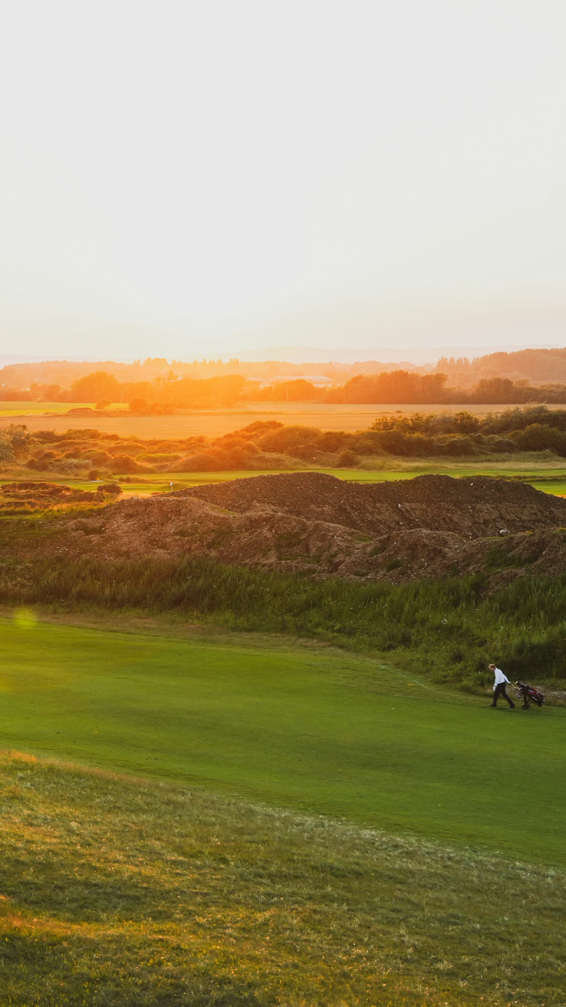 A golfer walking a fairway at sunset, generic stock photo pending real venue photography.